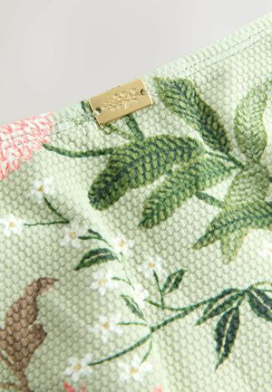Texturált világos zöld szövet virág- és levélmintákkal. Egy kis arany fémcímke van rajta, ami fokozza a dizájnt.