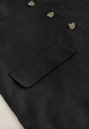 Mustast kangast, millel on sile tekstuur, kaunistatud kahe ümmarguse nupu ja klapiga tasku detailiga. Lihtne disain, sobib erinevate stiilide jaoks.