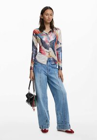 Overhemd met lange mouwen en knopen, met een kleurrijke abstracte print; heeft een getailleerd ontwerp. Gecombineerd met wijde blauwe jeans en rode schoenen.