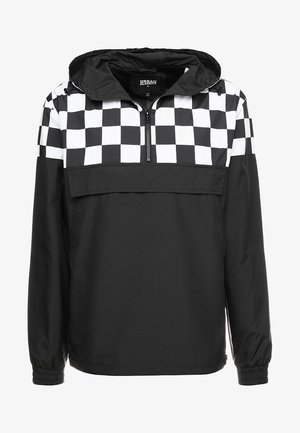 Chaqueta ligera negra con un patrón de cuadros en blanco y negro en la capucha y la parte superior delantera, que presenta un cierre de media cremallera y puños elásticos.