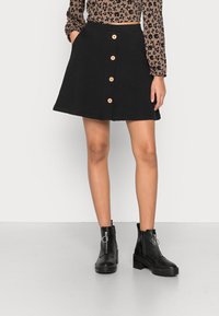 Saia A-line preta com cinco botões frontais e bolsos laterais. Combinada com botas ankle pretas com fecho lateral e detalhes em metal circular.