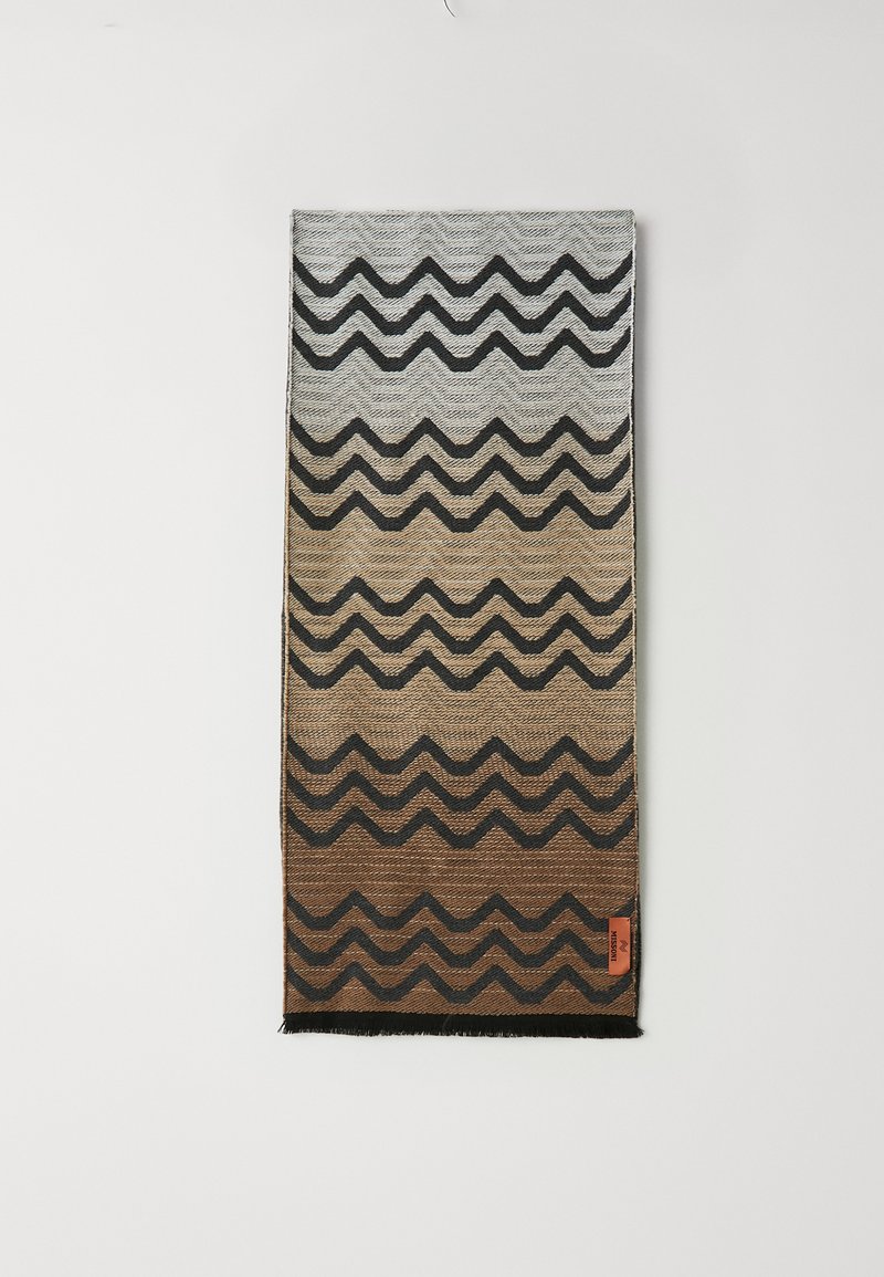 Sciarpa tessuta con un motivo zigzag sfumato nei toni del grigio, marrone e nero. Presenta bordi frangiati e un piccolo etichetta arancione in basso.