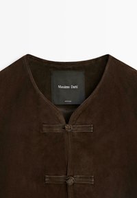 Veste en daim brun foncé avec encolure arrondie et deux boutons-pression en forme de nœud en cuir, avec une étiquette de marque "Massimo Dutti" à l'intérieur.