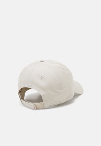 Beige baseball cap laget av bomull. Har en rund krone, sydd ventilasjonsåpninger og justerbar stropp bak.