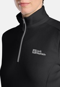 Czarny polarowy pulower z wysokim kołnierzem, przednim zamkiem błyskawicznym i szarym akcentem. Posiada małe haftowane logo na lewej części klatki piersiowej.