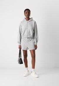 Felpa grigia in cotone con zip e vestibilità comoda, abbinata a pantaloni corti coordinati. Presenta polsini a costine, una vita elastica e sneakers bianche.