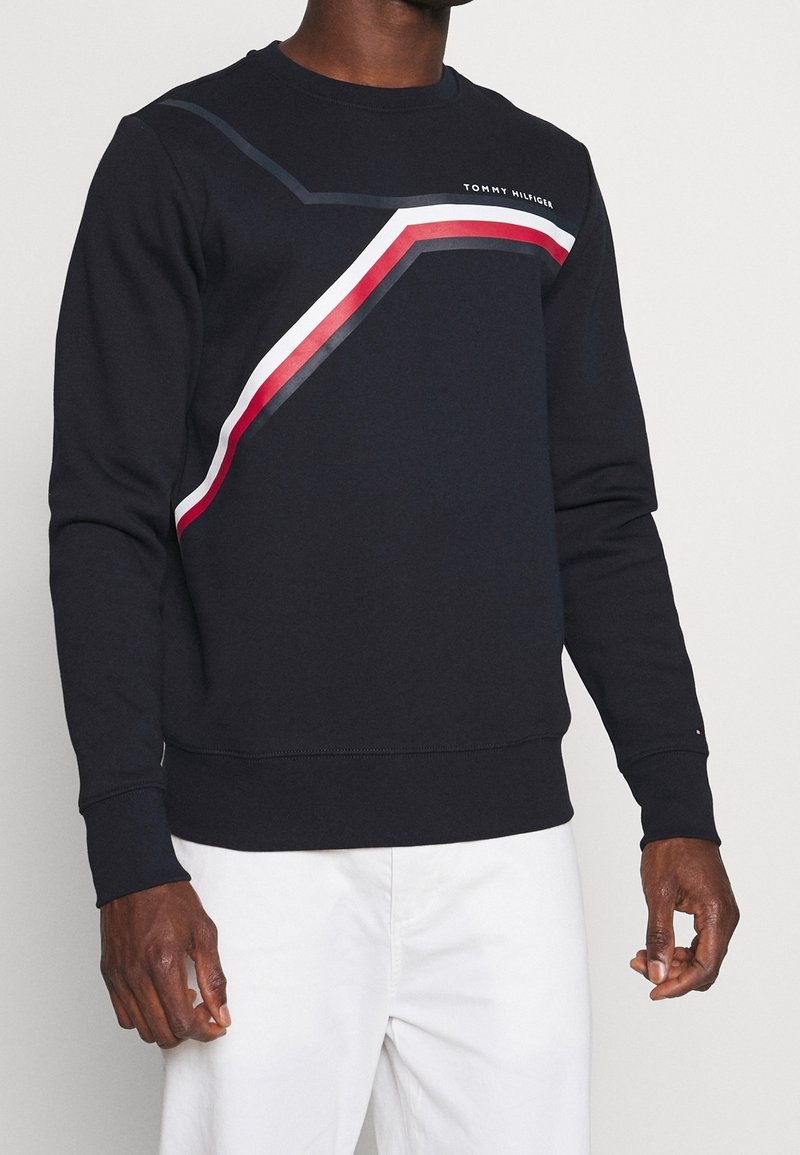 Navy crew neck sweatshirt made of cotton, featuring diagonal red and white stripes, and logo on the chest; ribbed cuffs and hem.