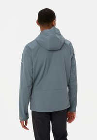 Veste imperméable grise avec une capuche, texture lisse, poignets élastiques et poches latérales, conçue pour une utilisation en extérieur, avec une coupe moderne et élégante.