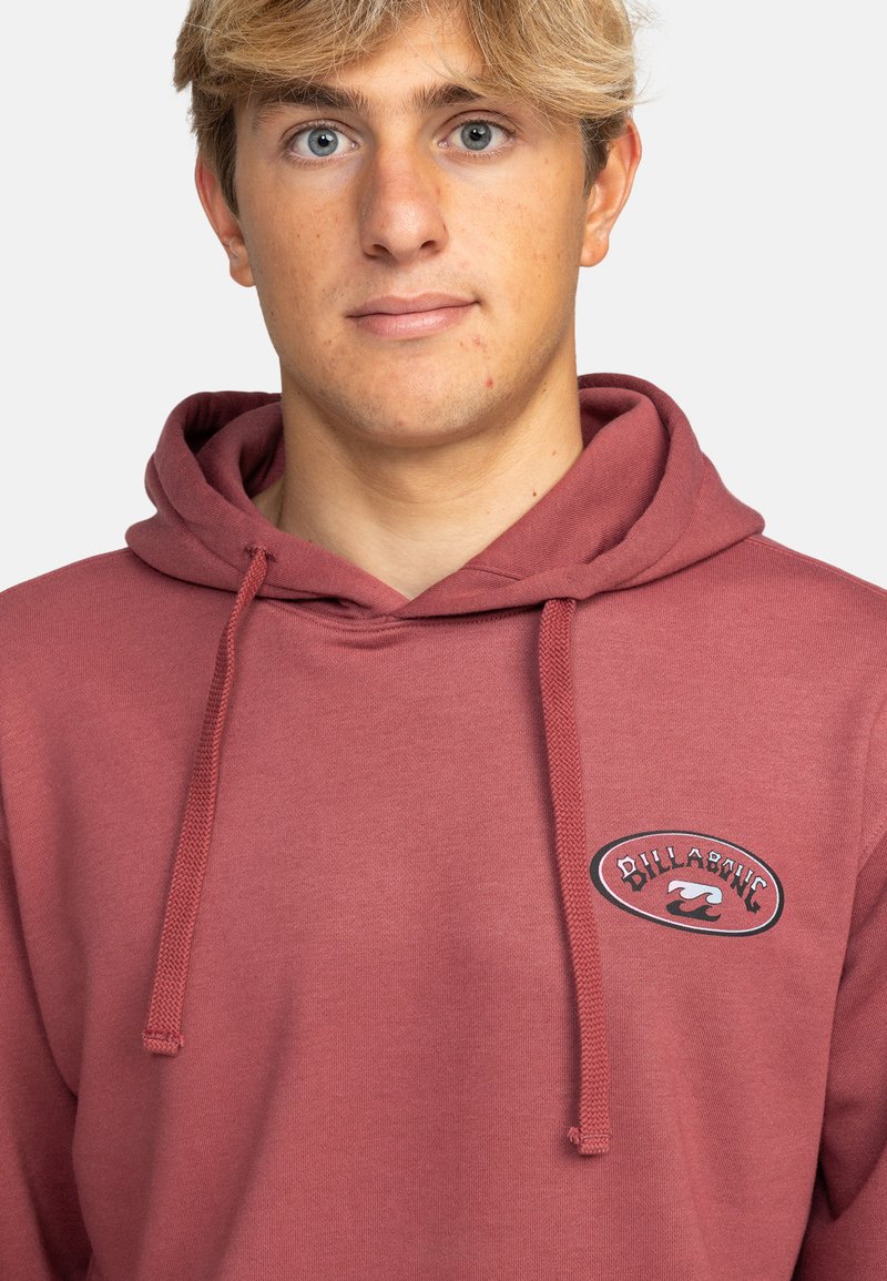 Sudadera marrón en tela suave con un parche de logo en el frontal. Presenta cordones ajustables, un bolsillo tipo canguro y puños acanalados.