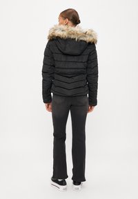 Casaco puffer preto com capuz de pelagem sintética destacável, riscas texturizadas, fecho de correr e punhos canelados, combinado com jeans escuros e sapatos de plataforma.