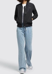 Černá bomber bunda se zipem vpředu, žebrovanými manžetami a pasem, kombinovaná s světle modrými širokými džíny a bílými teniskami.