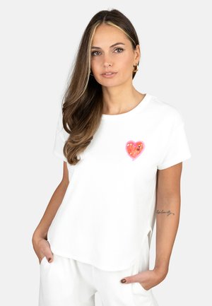 Weißes T-Shirt mit kurzen Ärmeln, rundem Ausschnitt und einer rosa Herzstickerei mit Pailletten auf der Brust. Weicher, glatter Stoff.