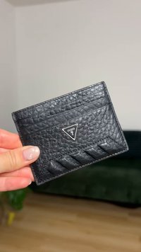 Black leather cardholder featuring a textured finish, multiple card slots, and a triangular silver logo. Measures approximately 10 cm by 7 cm.
