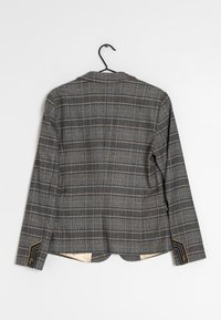 Plaid blazer in gray, black, and orange, featuring a textured fabric, notch lapels, and decorative accents on sleeve cuffs.