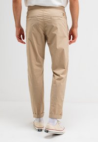 Beige, lichte cargobroek met een elastische tailleband, opgerolde boorden en twee achterzakken. De stof heeft een soepele textuur.