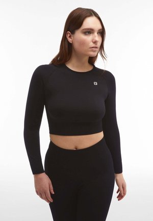 Musta pitkähihaisuus crop top, valmistettu joustavasta kankaasta, jossa on tiukka muotoilu ja pieni logo rinnassa. Sileä pinta, minimaalinen yksityiskohta.