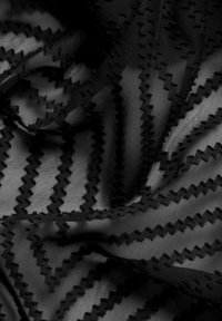Schwarzer Stoff mit transparenter Textur, der ein Zickzackmuster aus erhöhten Stichen aufweist. Das Material ist weich und leicht.