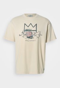 Μπεζ βαμβακερό T-shirt με γραφικό σχέδιο που απεικονίζει ένα στέμμα και αφηρημένα σχήματα σε μαύρο, ροζ και κόκκινο χρώμα. Κοντά μανίκια και στρογγυλή λαιμόκοψη.