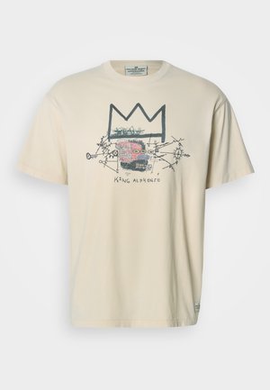 T-shirt en coton beige avec un motif graphique représentant une couronne et des formes abstraites en noir, rose et rouge. Manches courtes et col rond.
