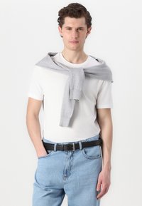 Siv sweater zavezan okoli vratu, bela majica s krožnim izrezom, modri denim kavbojke, črn pas. Enostavna vsakdanja obleka z svetlimi barvami in mehkimi teksturami.