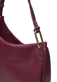 Borsa in pelle di un profondo borgogna, con una superficie liscia, forma arrotondata e dettagli in metallo dorato attaccati a una tracolla annodata.