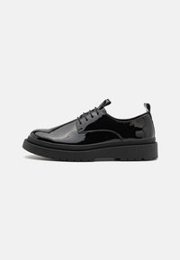 Zapatos de charol negro con cordones, con una gruesa suela de goma negra, que presentan una puntera redondeada y sutiles acentos de costura.