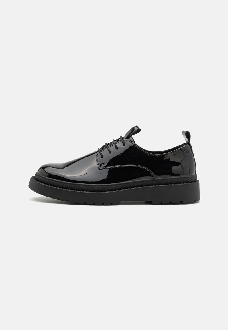 Zapatos de charol negro con cordones, con una gruesa suela de goma negra, que presentan una puntera redondeada y sutiles acentos de costura.