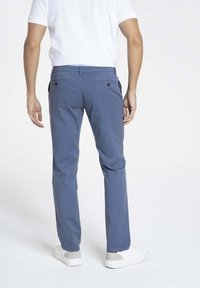 Chinos bleus en tissu léger, coupe droite, poches arrière avec bouton, portés avec des baskets blanches et une chemise blanche ajustée.