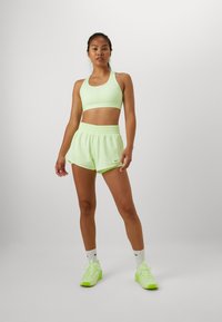 Soutien-gorge de sport vert clair et shorts assortis, tous deux en matériau extensible. Logo Nike blanc sur le soutien-gorge et les shorts. Baskets jaune-vert vif.