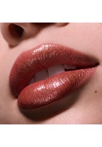 Kiiltävät huulet lämpimällä, metallinhohtoisella ruusuharmaalla sävyllä, joissa on sileä rakenne ja hienostuneet kimalteet. Taustalla luonnollinen ihonväri.