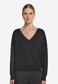 Svart långärmad tröja med V-ringning, tillverkad av mjukt tyg. Har avslappnad passform och ribbad nederkant. Enkel, minimalistisk stil.