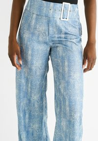 Blue textured trousers with a wide fit, featuring a high waistband and a rectangular white belt buckle with silver accents.