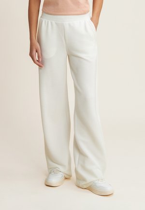 Pantaloni della tuta bianchi a coste con vestibilità rilassata, dotati di tasche laterali e una cintura elastica, abbinati a sneaker chiare.