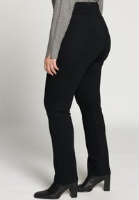 Schwarze Stretchhosen mit hoher Taille, glatter Textur und maßgeschneidertem Schnitt. Kombiniert mit schwarzen Stiefeletten mit Absatz und einem grauen Langarmoberteil.
