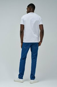 Camiseta blanca de manga corta, vaqueros azules y zapatillas blancas. Diseño sencillo, material de algodón, corte holgado y cuello redondo estándar.
