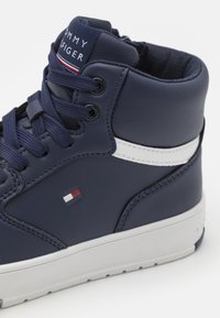 Mörkblå höga sneakers i läder med slät yta, vit sidostrimma, rund tå och en logotypapplikation med röda och vita accenter på tungan.