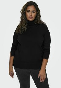 Črna turtleneck pulover s rebrastimi manšetami in robom. Mehak material, sproščen kroj, z bočnimi razporki za dodatno gibljivost. Uporabljen z temnimi džinsom.