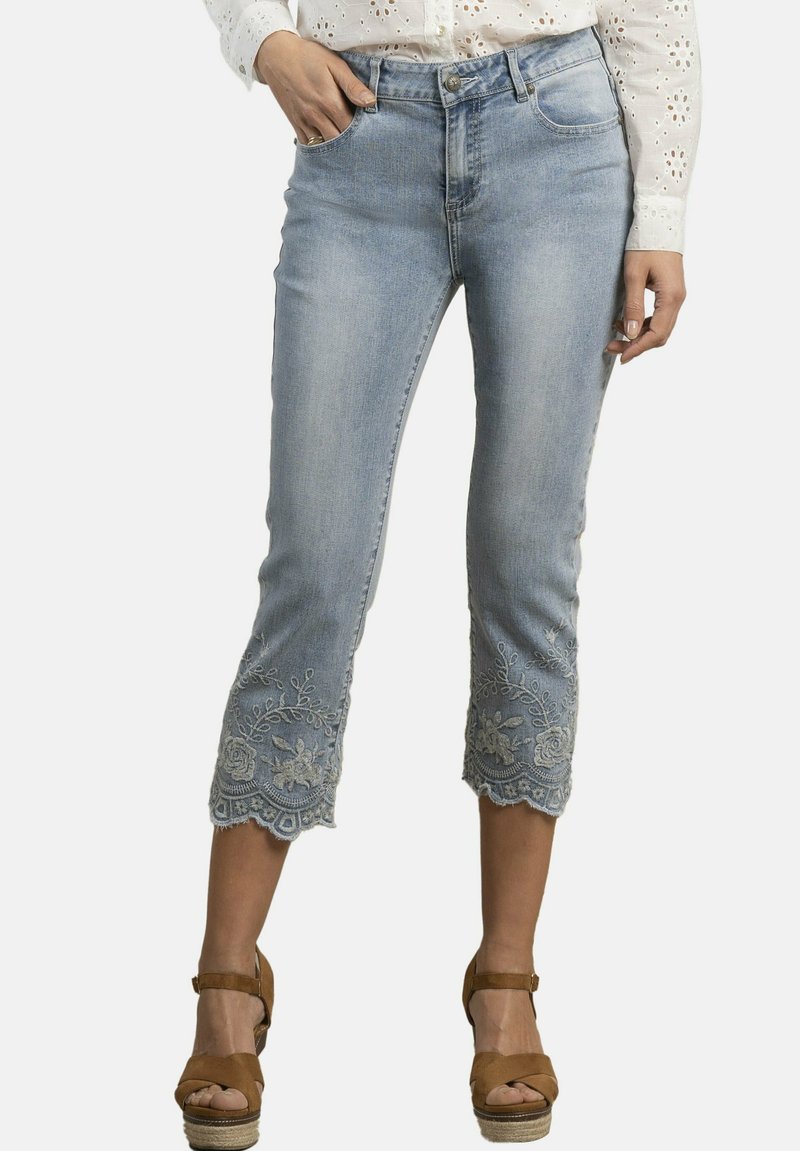 Los vaqueros cortos de color azul claro presentan delicados bordados de encaje en el dobladillo, cinco bolsillos y un cierre clásico con botón y cremallera.