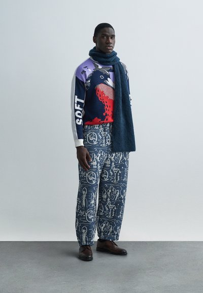 Πλεκτό πουλόβερ με μοτίβα σε μωβ, κόκκινο και ναυτικό μπλε; φαρδιά μπλε κασκόλ; φαρδιά, μοτίβο παντελόνια σε ναυτικό μπλε; καφέ δερμάτινα παπούτσια.