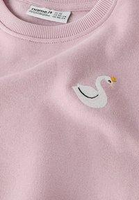 Felpa rosa chiaro con un piccolo cigno bianco ricamato, decorato con una corona gialla e dettagli neri. Tessuto morbido con scollatura a coste.