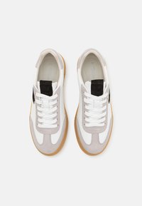 Paire de baskets blanches et gris avec semelles en gomme et languettes noires au talon, vues de dessus sur un fond blanc.