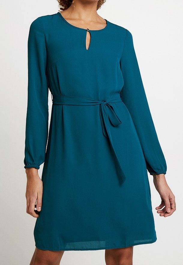 Robe sarcelle à manches longues longueur genou avec ceinture nouée à la taille et petite fermeture par bouton à l'encolure en forme de goutte sur une femme.