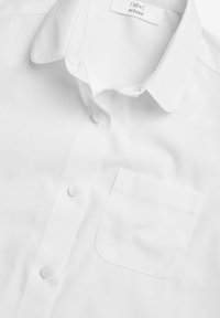 Camicia bianca con colletto, realizzata in tessuto soffice, dotata di una tasca applicata e sei bottoni sulla parte anteriore, con un design classico e semplice.