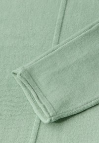 Suéter verde claro con un tejido suave y texturizado, con costuras ligeramente cosidas y detalles de puños acanalados.