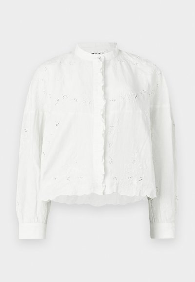Fehér blúz fodros gallérral, hosszú ujjakkal és gombos záródással. Virágos hímzéssel és rövid, texturált dizájnnal.