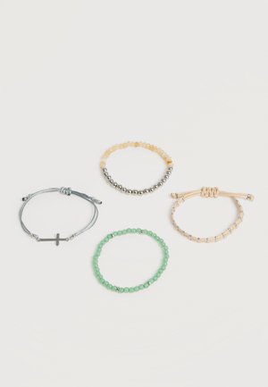 Quattro braccialetti su una superficie bianca: uno grigio con una croce, uno con perline gialle e argento miste, uno beige con dettagli argentati e uno verde con perline.