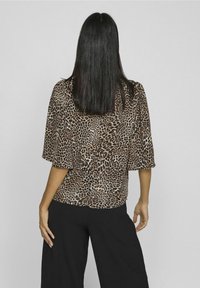 Blusa con stampa leopardata, maniche ampie e orlo arrotondato, realizzata in tessuto leggero, abbinata a pantaloni neri a gamba larga.