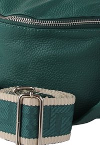 Turquoise leren tas met ritssluiting en een gestructureerde afwerking. Voorzien van een patroonriem in turquoise en crèmekleur met een zilverkleurige metalen gesp.