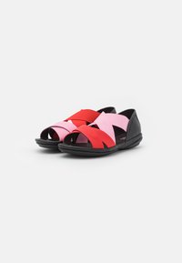 Svarta sandaler med korsade remmar i röd och rosa elastisk material. Har en öppen tå-design och dämpad sula för komfort.