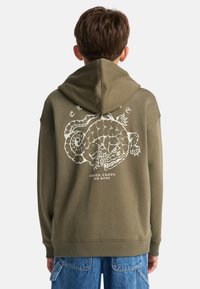 Felpa verde oliva con un design grafico bianco di una creatura sulla schiena. Presenta una tasca a marsupio e polsini e orlo a costine.